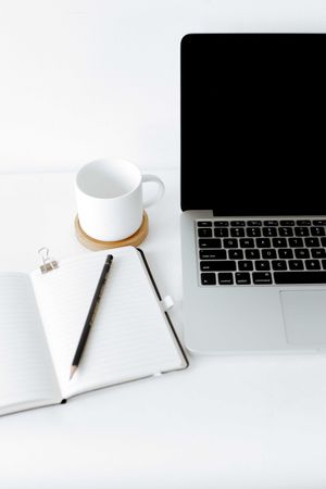 MacBook pro beside mug, pen and notebook
