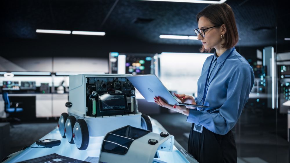 Portrait of a Female Engineer Using a Laptop While Developing a Remotely Controlled Delivery Robot.Technical Specialist Working in High Tech Research Laboratory with Modern Equipment