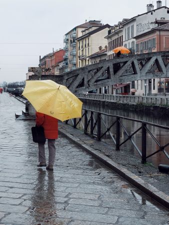 Person in red coat holding yellow umbrella walking on sidewalk