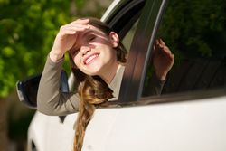 A Joyful Young Woman Happily Enjoying a Ride in a Car Under a Bright and Sunny Day