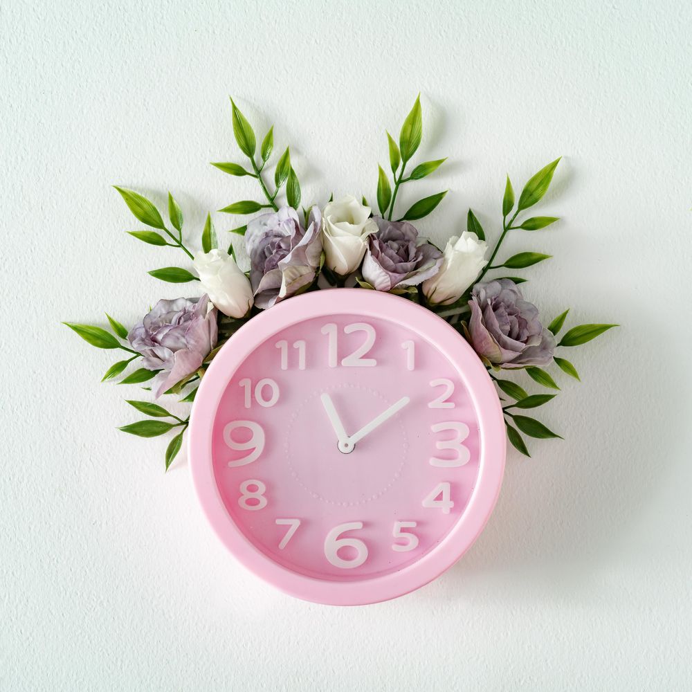 Pink clock with flowers and leaves on light  background