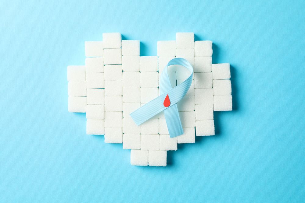 Diabetes awareness ribbon and heart made of sugar cubes on blue background