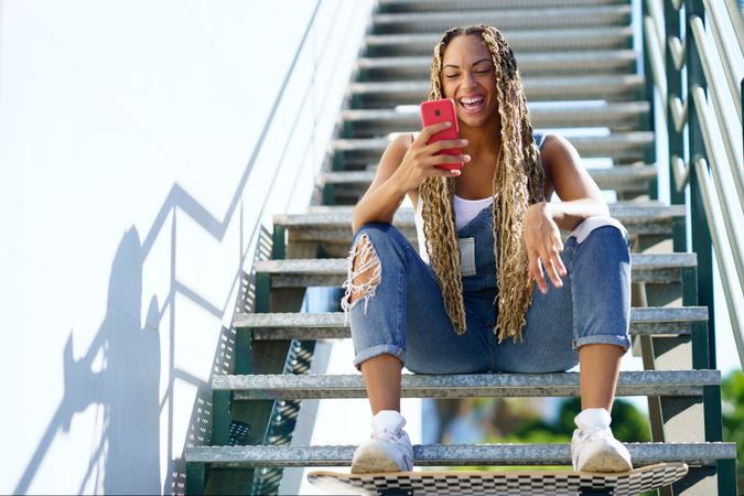 Laughing female skater checking phone on stairs, copy space