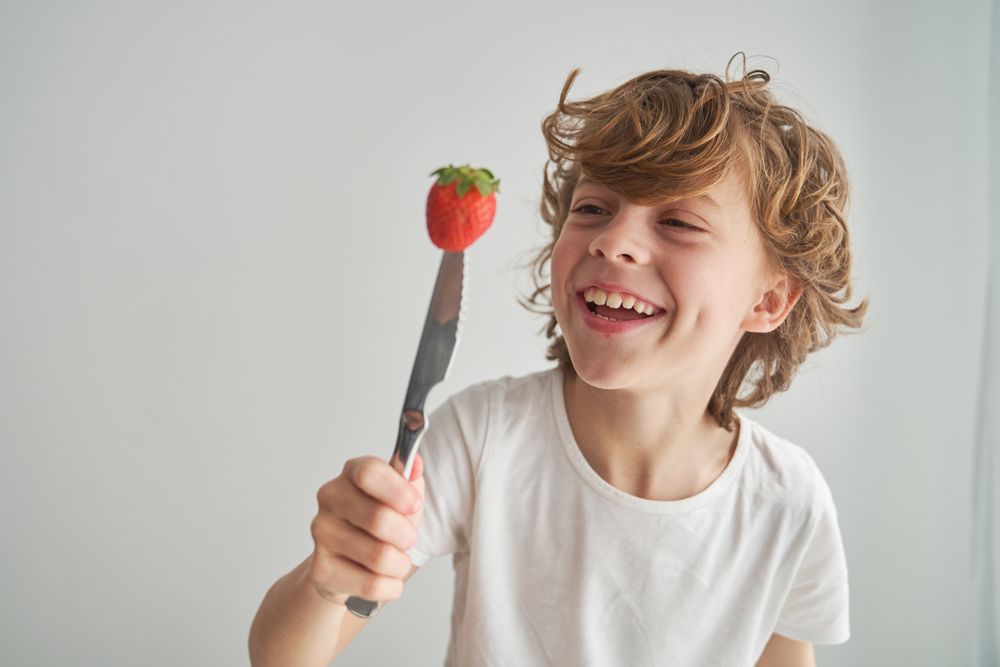 Cheerful boy looking at knife with strawberry on top