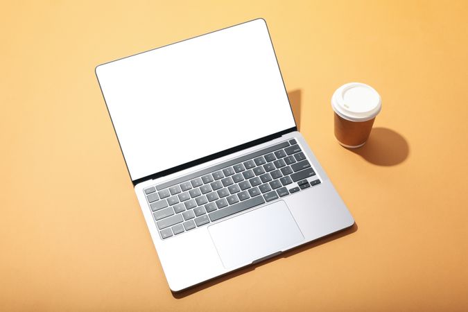 Top view of laptop with mockup screen and to go coffee on light orange desk