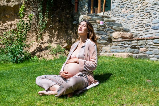 Pregnant woman sitting in the sun on the grass