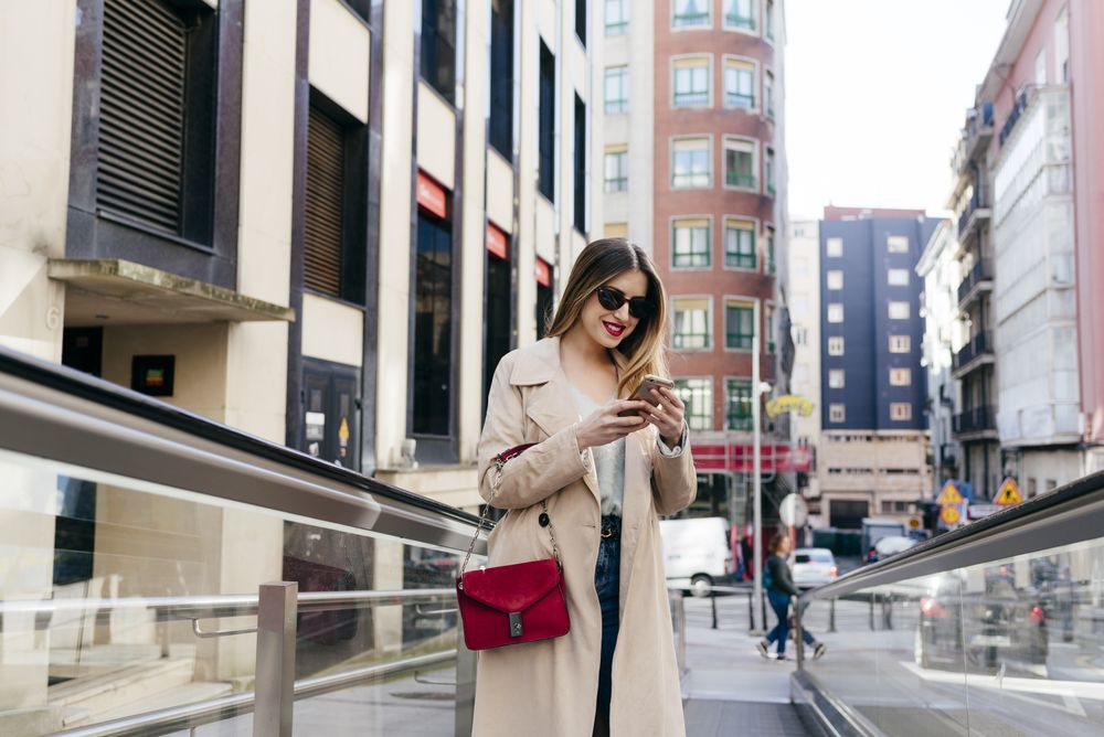 Young cheerful female walking on street with smartphone