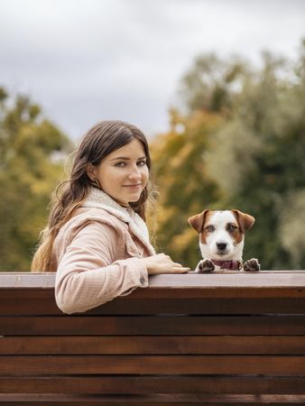 Woman and a dog sitting on wooden bench outdoor in the park