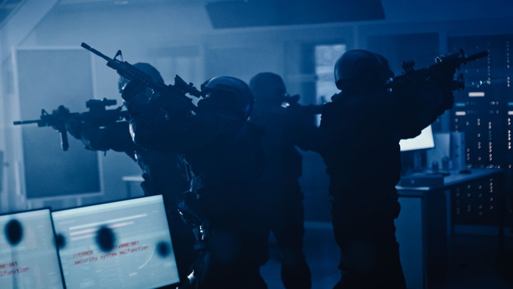 Masked Squad of Armed SWAT Police Officers Stand in Dark Seized Office Building with Desks and Computers.