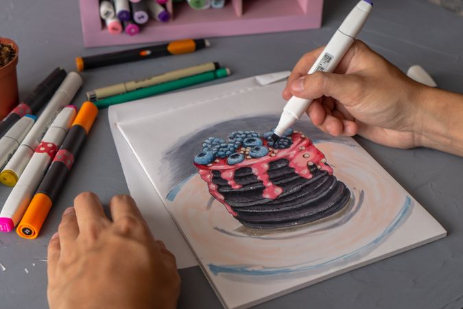 Person painting a layered pancakes with berries using markers
