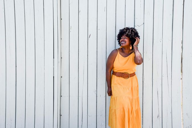 Woman in orange sleeveless dress standing beside wall