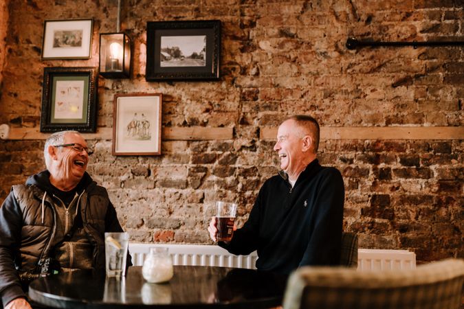 Two mature men laughing over drinks at a pub