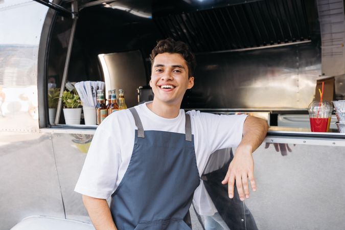Male in apron happily leaning in window of food truck