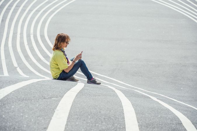 Modern relaxed woman on marked road and browsing smartphone