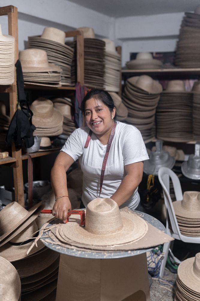 An adult Hispanic woman is smiling while working in a hat workshop