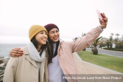 Two young Asian women in winter clothes take funny selfie 0LL1e0