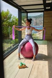 Sportswoman doing exercises for arms while sitting on fitness ball in studio