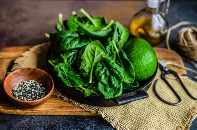 Fresh spinach & avocado on board with bowl of seasonings