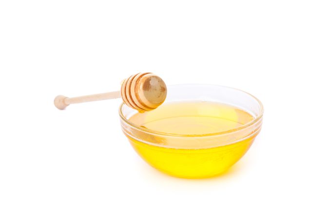 Dipper and honey in glass bowl isolated on plain background