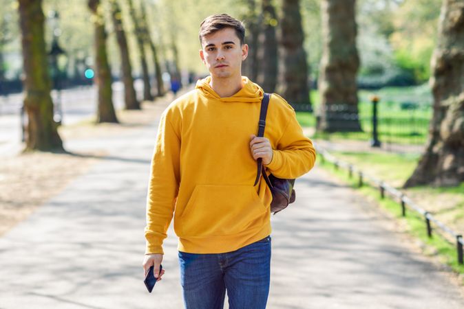 Man in yellow hoodie with backpack walking in park