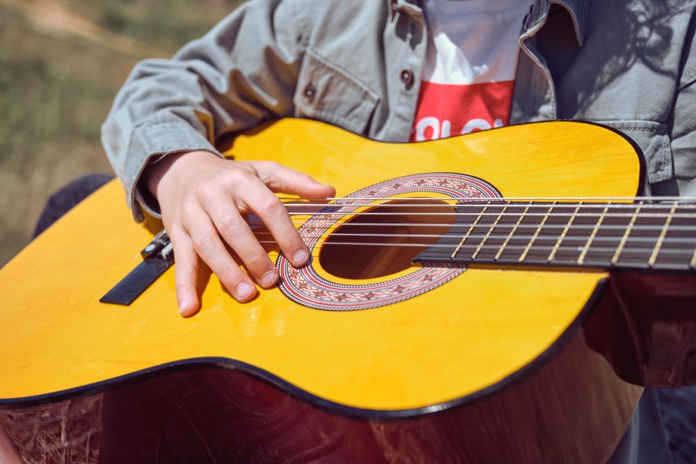 Crop unrecognizable child playing guitar in nature