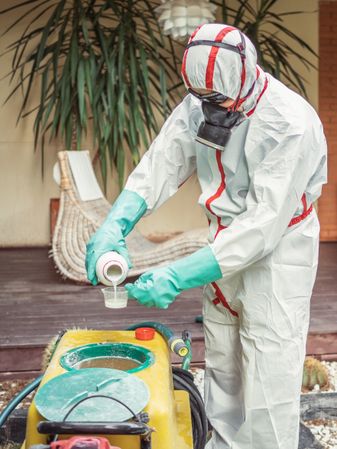 Man in suit for fumigation pouring chemical into tank