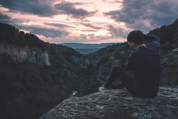 man with photo camera sitting on hill mountain with magnificent sunset