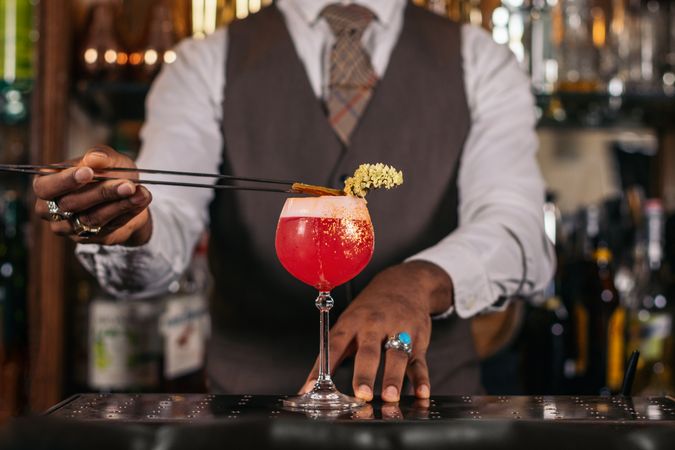 Close-up of an unrecognizable Black bartender pouring a cocktail and decorating it with garnish