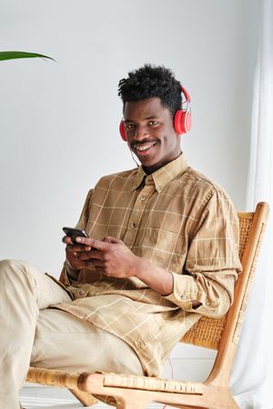 Smiling Black man in headphones with smartphone on white background