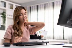 Asian woman sitting in office and holding her painful neck