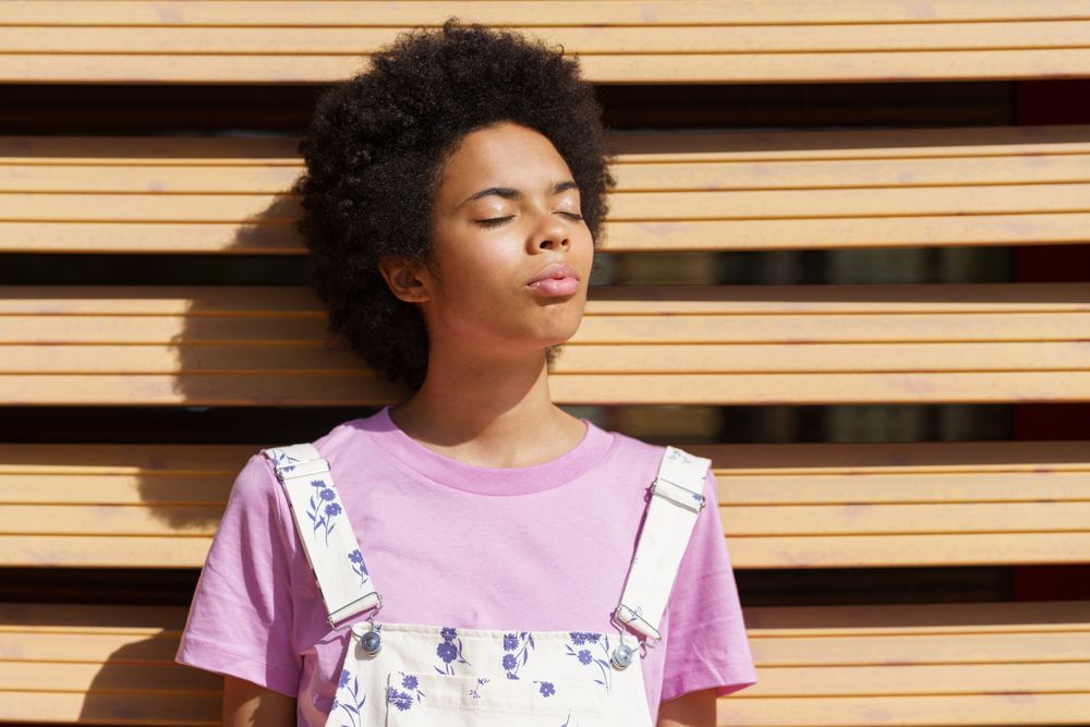 Female leaning on wooden shutters facing the sun with eyes closed
