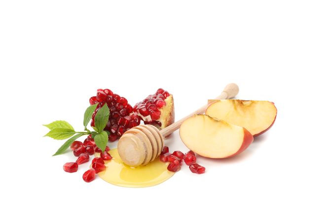 Honey dipper, open pomegranate, mint, and apple quarters centered on plain table