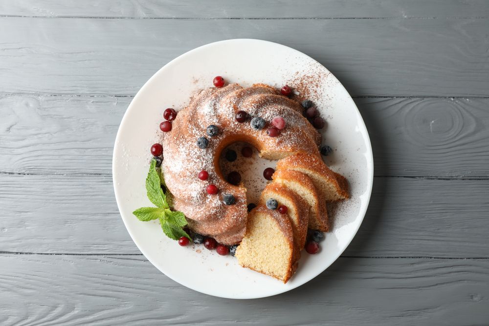 Cake with powdered sugar, berries and mint on wooden background, top view
