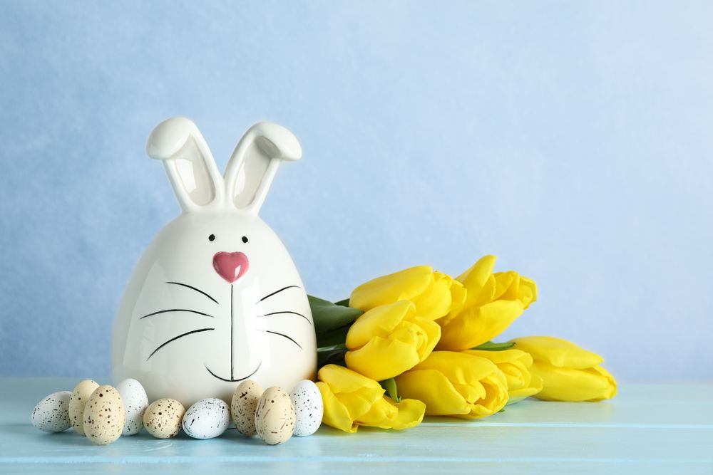 Decorated bunny and Easter eggs on table against color background. Space for text