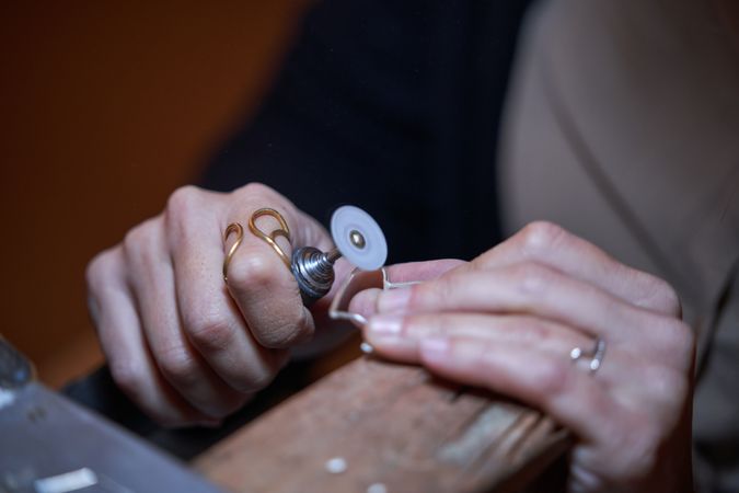 Crop anonymous jeweler using polisher during work at bench