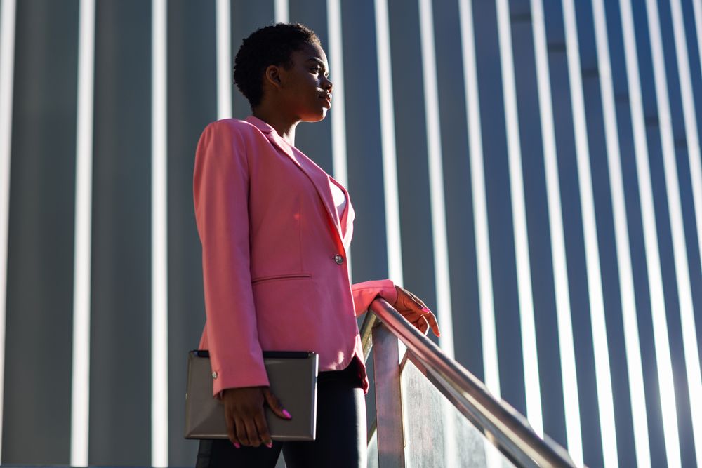 Female wearing suit with pink jacket outside office with striped shadows