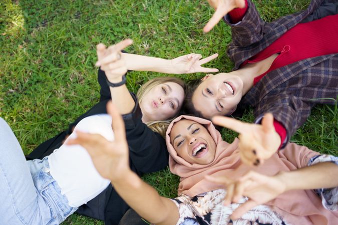 Looking down at three friends lying on grass smiling