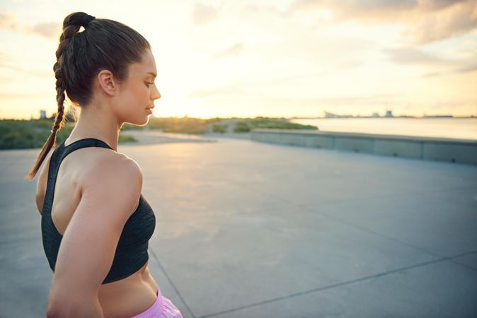 Athletic woman in sports bra and pony tail looking down in morning light