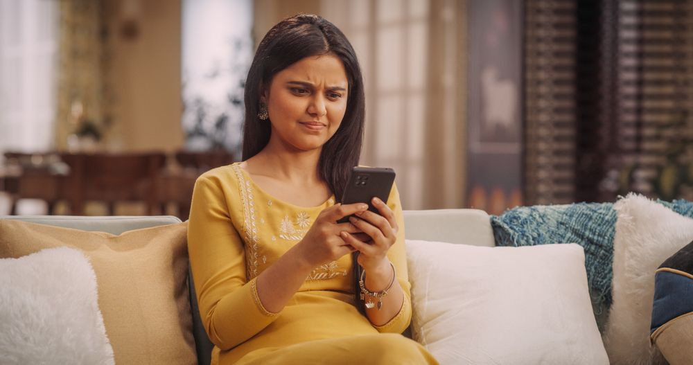 Portrait of a Confused Young Indian Woman Looking at her Smartphone, Reading the News in her Fancy Home