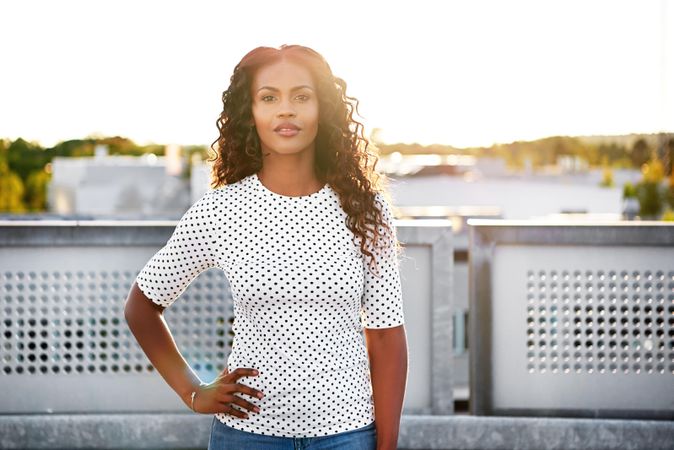 Confident Black woman standing on sunny roof top with hand on hip