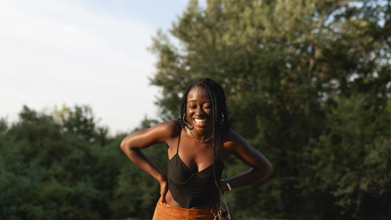 A young Black woman with braids in her hair laughs during a walk in the park at sunset