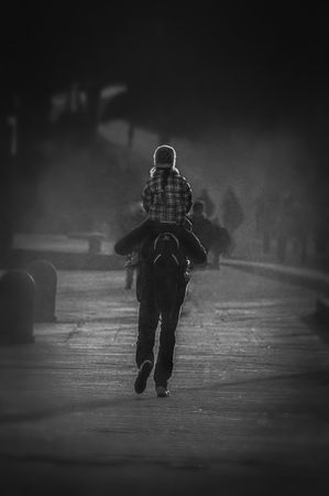 Back view of father holding daughter on his back walking on the road in grayscale