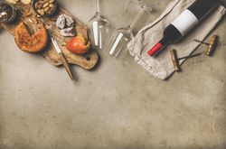 Cheese plate with red bottle of wine on linen towel, cork screws, glassware, with copy space
