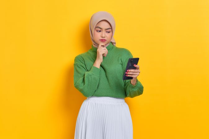 Woman in headscarf holding smart phone and reading something questionable