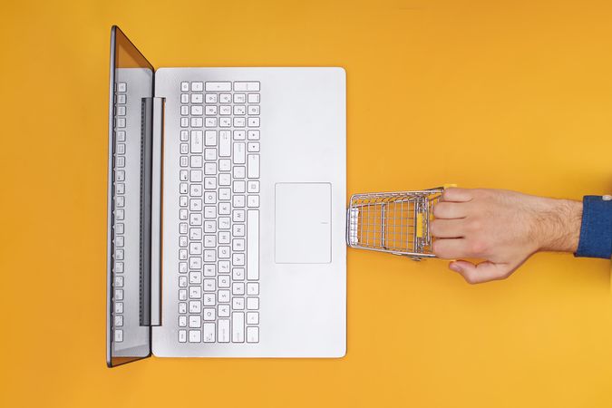 Online Shopping Concept with Laptop and Shopping Cart on Yellow Background