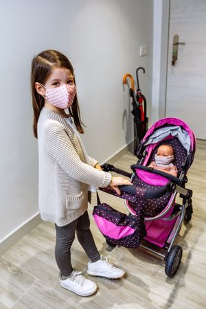 Girl with face mask ready to go for a walk with her doll with mask