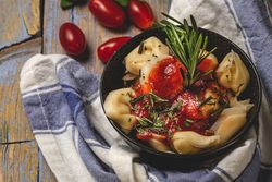Bowl of delicious ravioli with tomato sauce and rosemary on shabby table