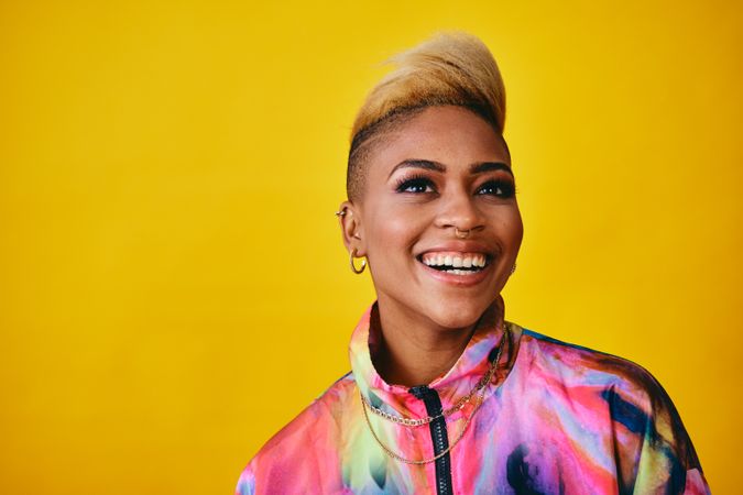 Studio shot of laughing Black woman in bold windbreaker jacket and gold jewelry looking away