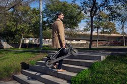 Stylish man with electric scooter walking up stairway in park