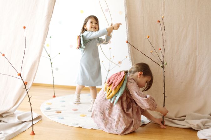 Happy little girls playing with sticks on wooden floor by white curtain
